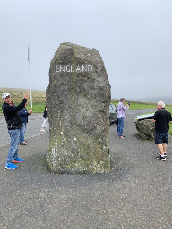 Des gens rassemblés autour d'une grande pierre dressée sur laquelle le mot « ANGLETERRE » est gravé.