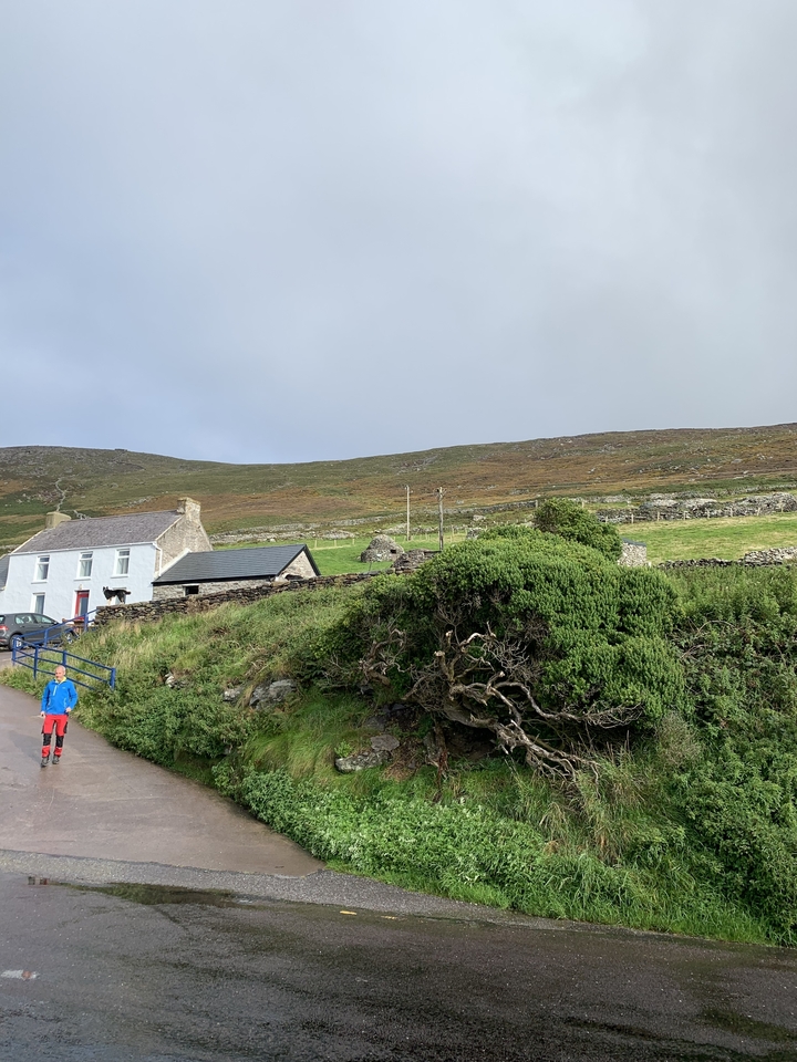 Une scène de campagne avec une maison, des murs de pierre, et une personne qui marche.