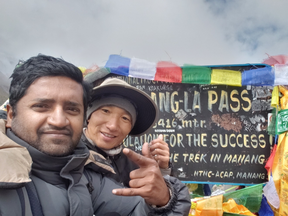Deux personnes prenant un selfie devant un panneau indiquant « Col de Thorong-La ».