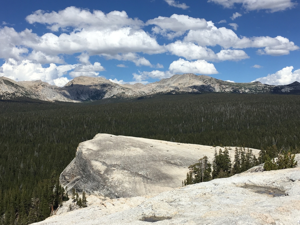 Dômes de granit avec une zone boisée en contrebas et un ciel tacheté de nuages.