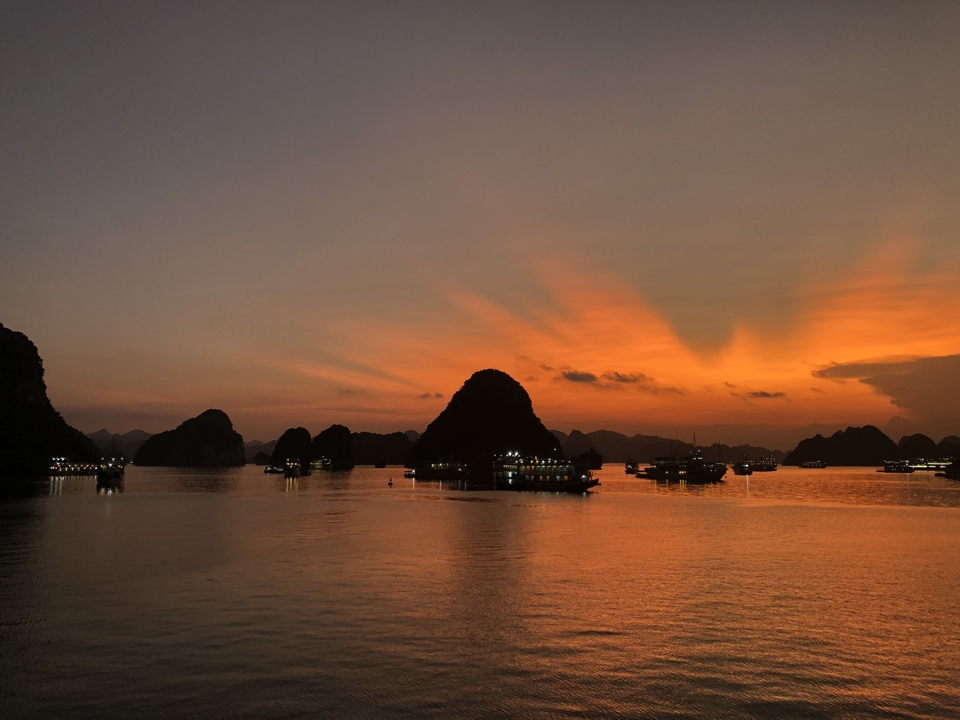 Bateaux dans la baie d'Halong au coucher du soleil avec des îles en silhouette.