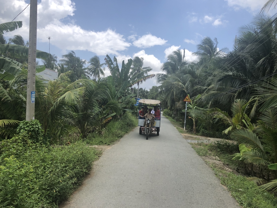 Des personnes voyageant dans un pousse-pousse motorisé sur une route étroite bordée de palmiers.