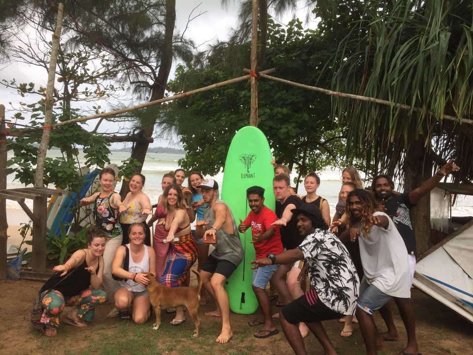 Groupe de personnes posant avec une planche de surf sur une plage.