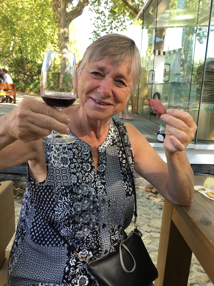 Une femme savoure un verre de vin et un morceau de charcuterie devant un magasin.
