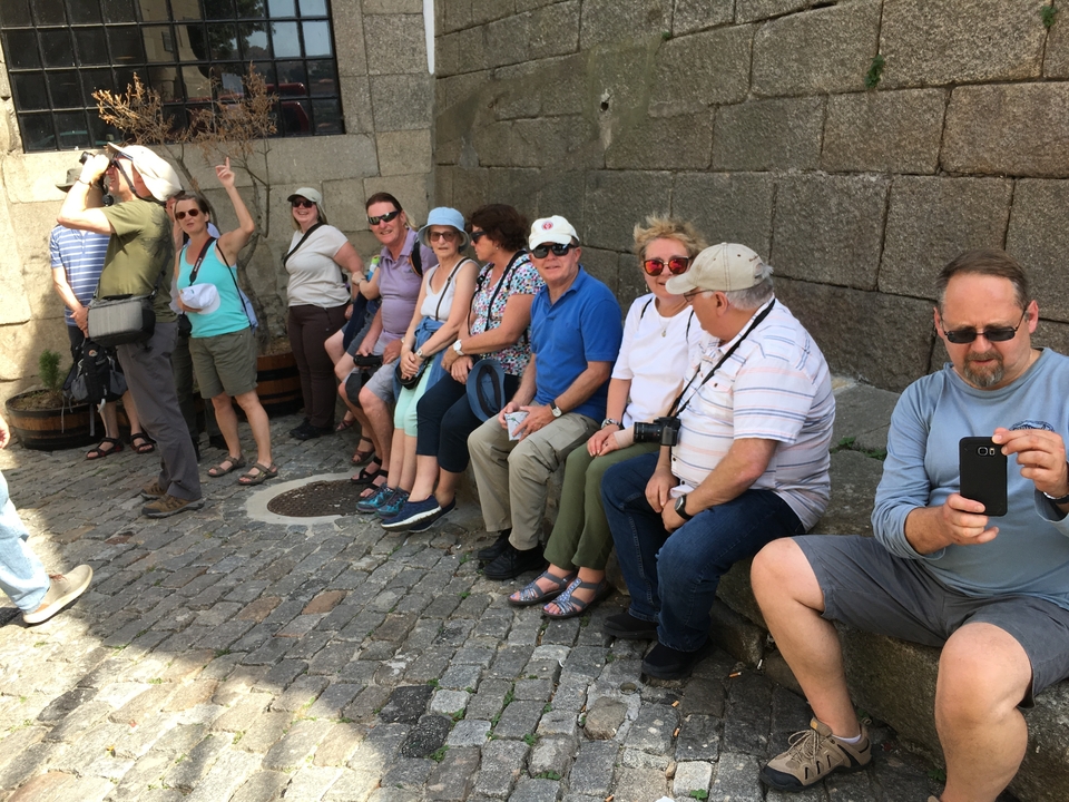 Un groupe de touristes assis sur des marches le long d'un mur de pierre dans un cadre extérieur.