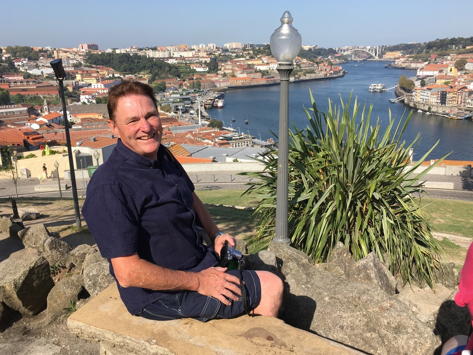 Un homme assis avec une vue de la ville et de la rivière derrière lui.