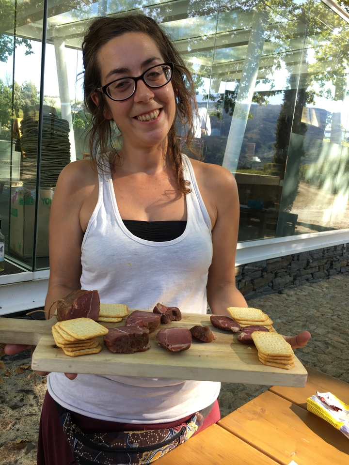 Une femme tenant une assiette de viandes et de crackers avec en arrière-plan une fenêtre en verre et un mur de pierre.