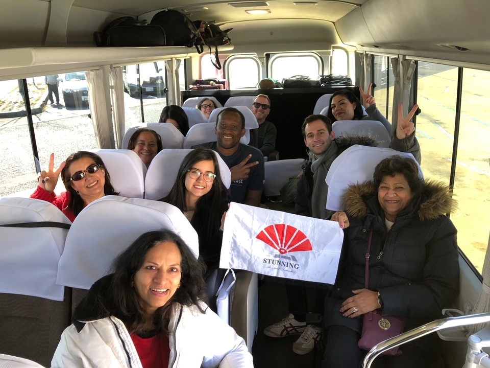 Groupe de personnes à l'intérieur d'un autocar de tourisme tenant un drapeau avec un motif d'éventail rouge.