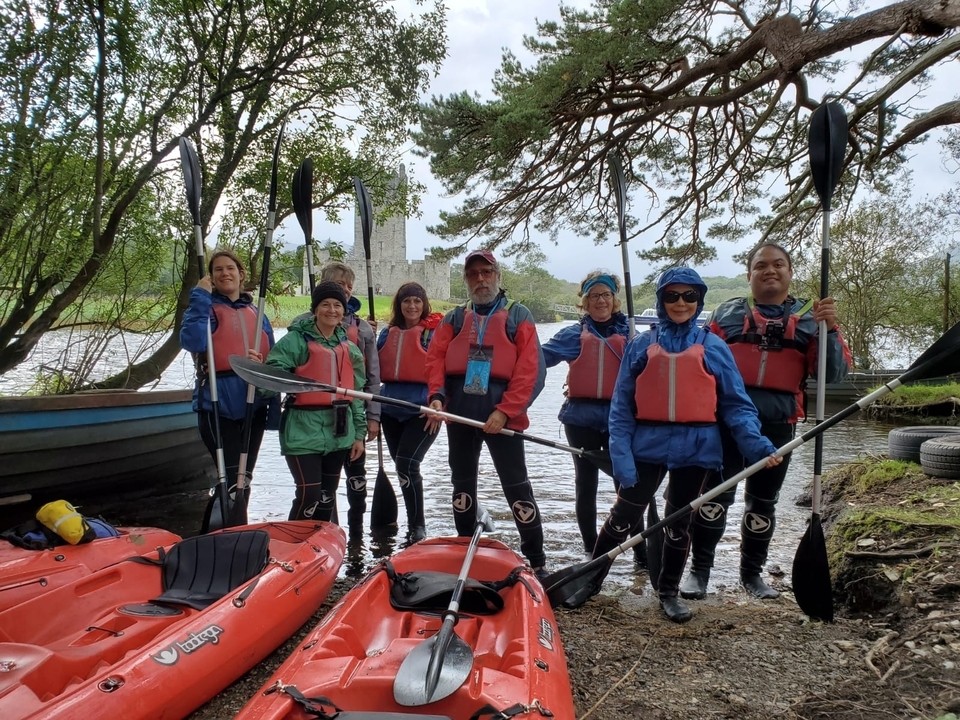 Group of people in kayak gear by the water with a castle in the background.
