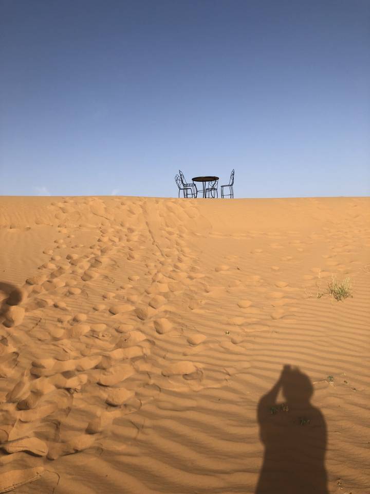 Deux chaises sur une dune de sable sous un ciel bleu clair.