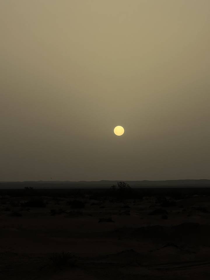 Un soleil se couchant sur un paysage aride avec un ciel dégagé.