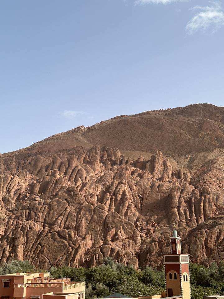 Une falaise rocheuse avec une tour de mosquée sous un ciel bleu dégagé.