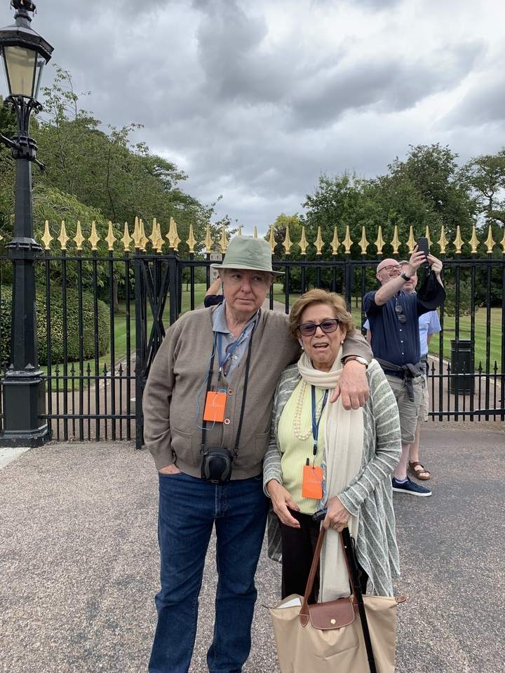 Couple posant devant des grilles ornées dans un parc.
