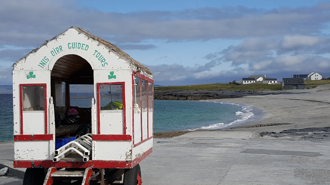 Un chariot de visite guidée à côté d'une plage avec des maisons au loin.