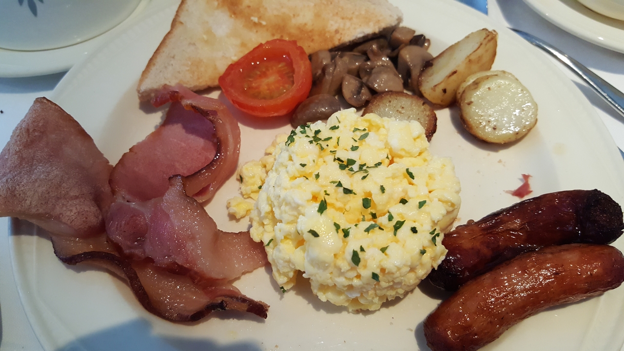 Une assiette avec des œufs brouillés, du pain grillé, du bacon et des saucisses.