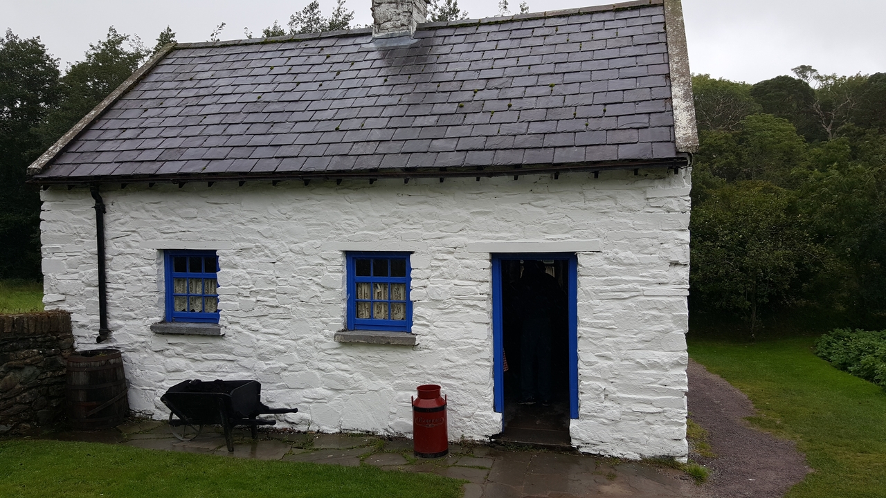 Cottage en pierre blanche avec des fenêtres bleues et un tonneau rouge.