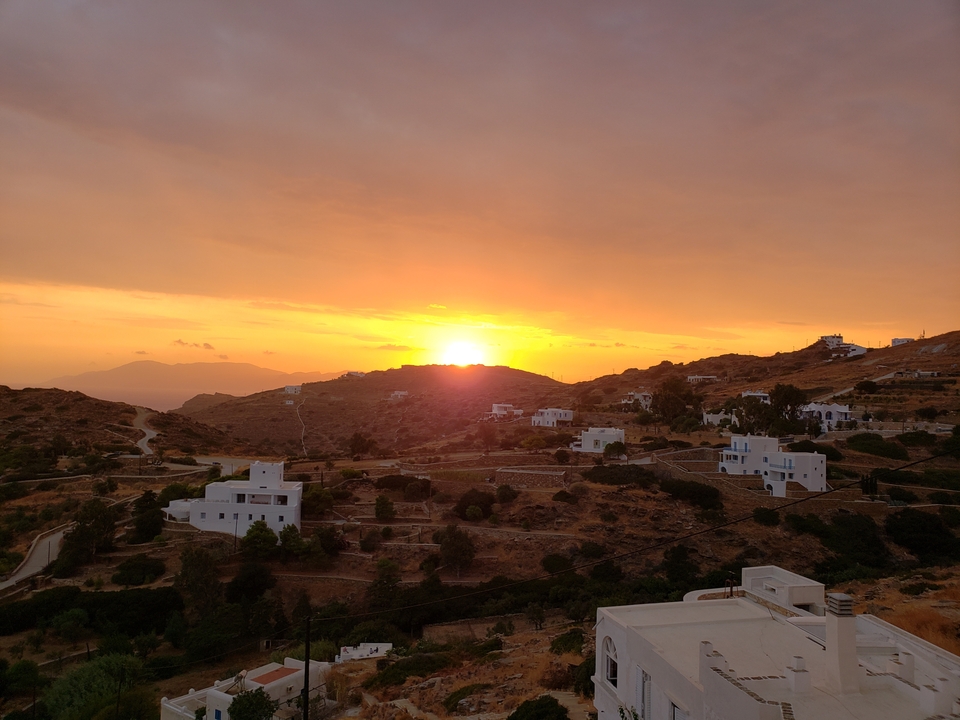 Coucher de soleil sur un paysage vallonné avec des maisons dispersées.