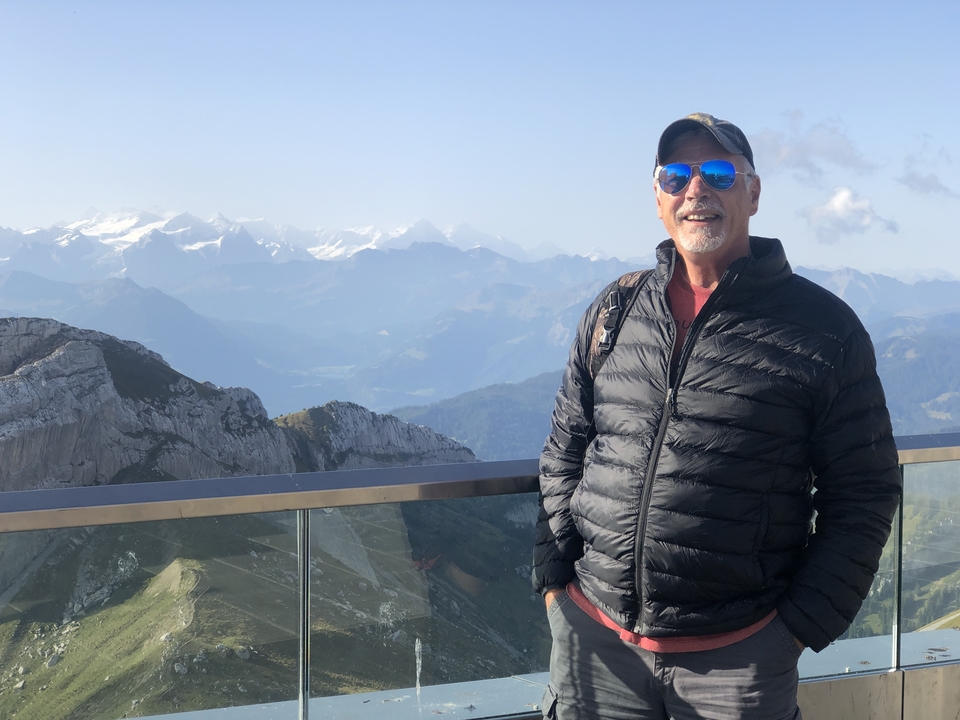 Homme debout sur une plateforme avec une vue alpine en arrière-plan.