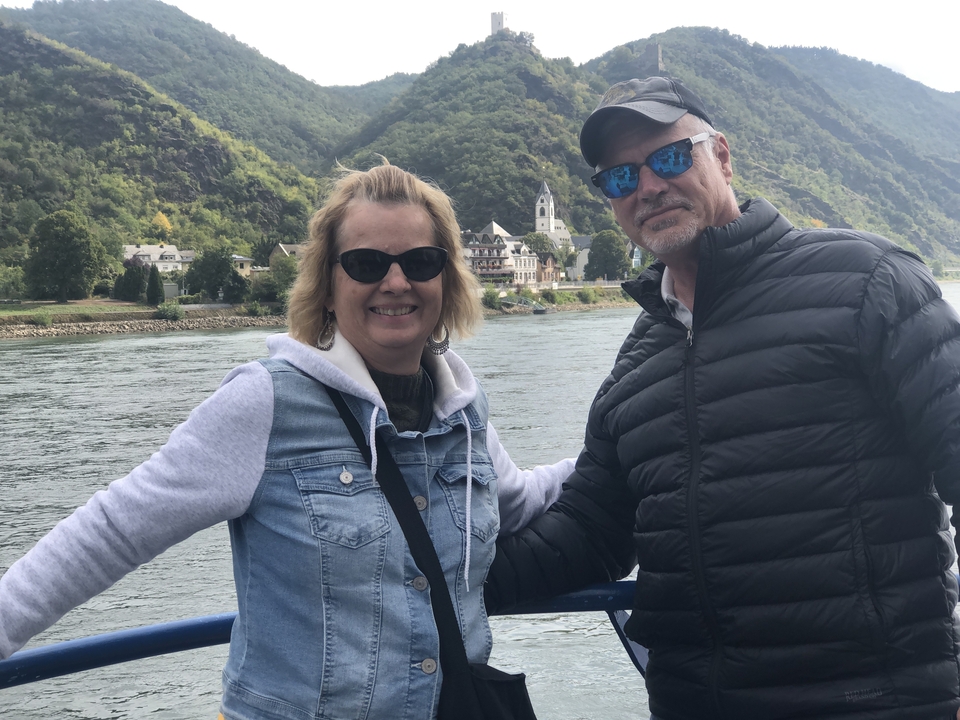 Deux personnes posant avec une rivière pittoresque et un village en arrière-plan.