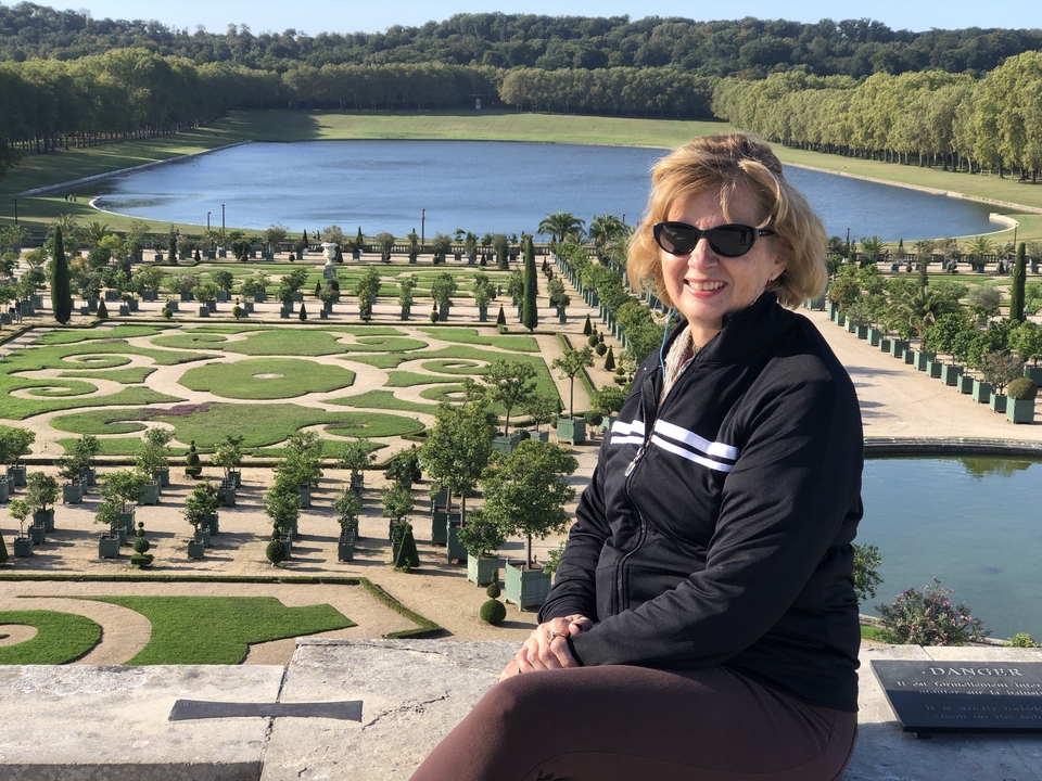 Femme assise avec un jardin à la française et des jeux d'eau en arrière-plan.