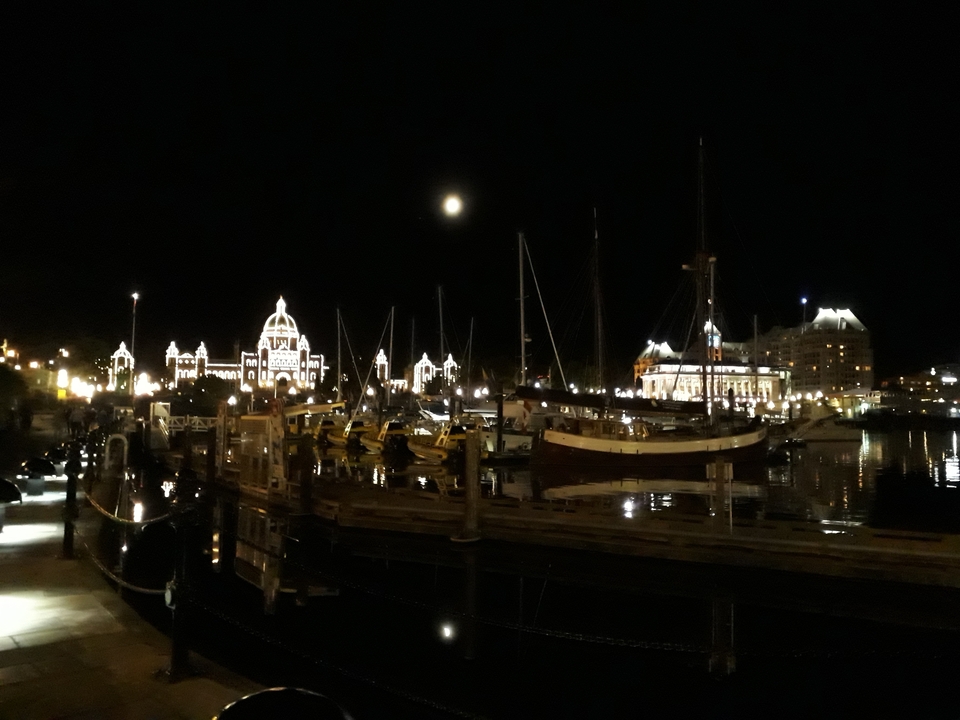 Scène nocturne avec des bâtiments illuminés et des bateaux dans le port.