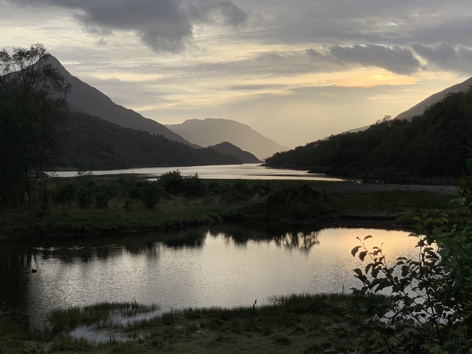 Eau calme reflétant les collines environnantes au coucher du soleil.
