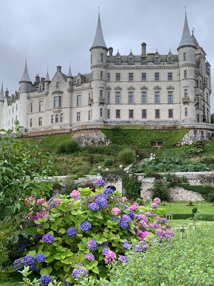 Château pittoresque avec jardins et fleurs colorées le long de la colline.