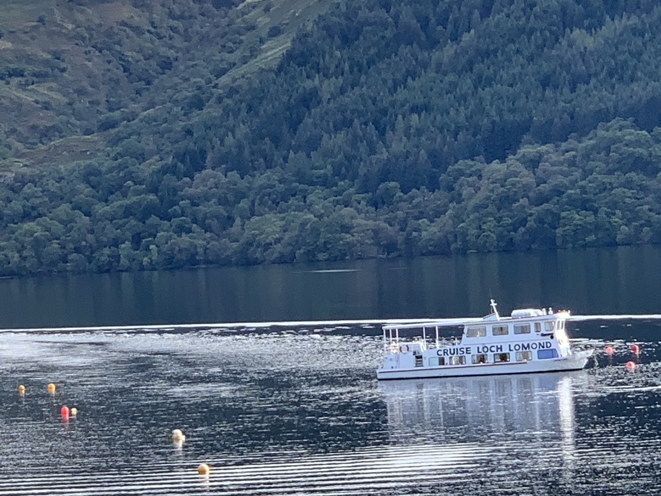 Bateau nommé 'CRUISE LOCH LOMOND' glissant sur une étendue d'eau calme entourée de forêt.
