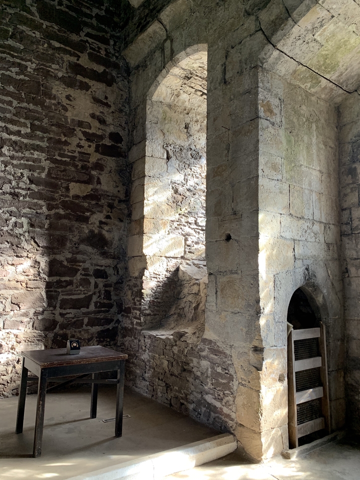 Intérieur d'un bâtiment en pierre avec des murs et des arches éclairés par le soleil.