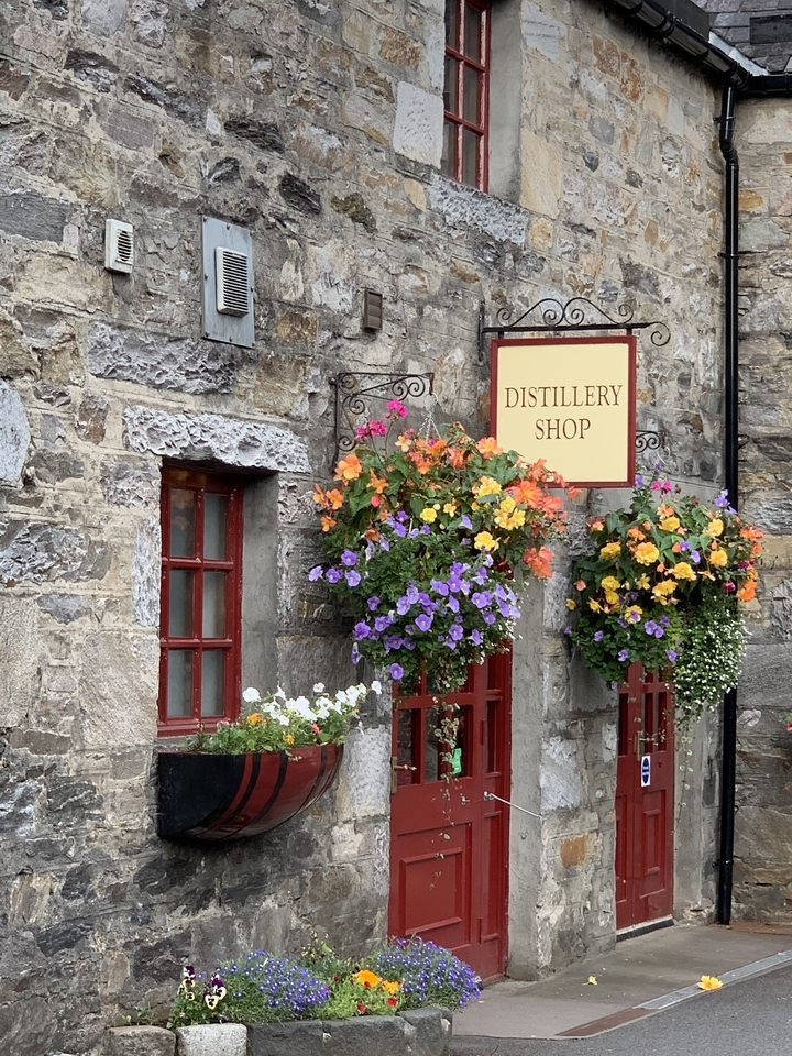 Enseigne de magasin de distillerie montée sur un bâtiment en pierre avec des fleurs colorées.