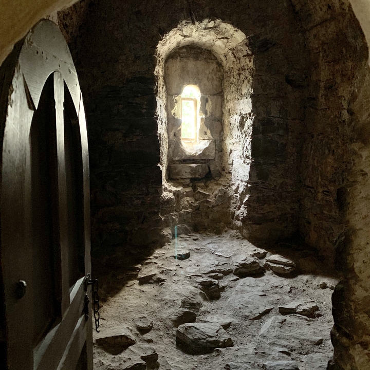 Intérieur de pierre faiblement éclairé avec une petite fenêtre à barreaux créant une atmosphère mystérieuse.