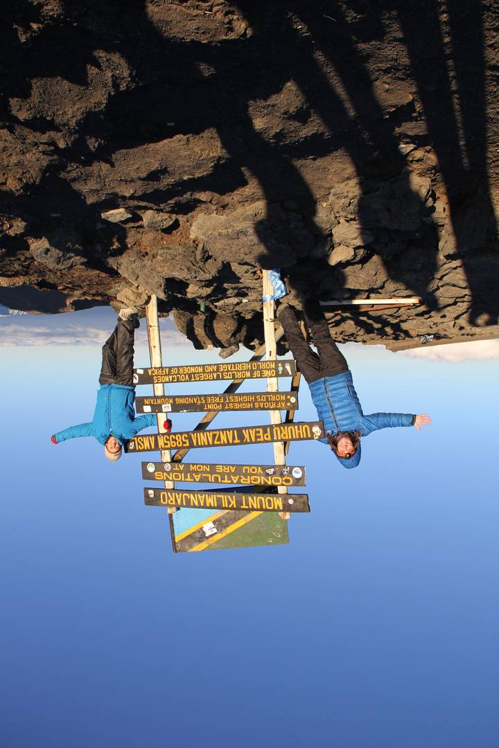 Two people celebrating at the summit of Mount Kilimanjaro with a sign.