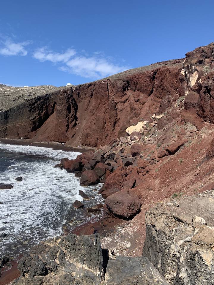 Côte avec des falaises rocheuses rouges et des vagues qui se brisent contre le rivage.