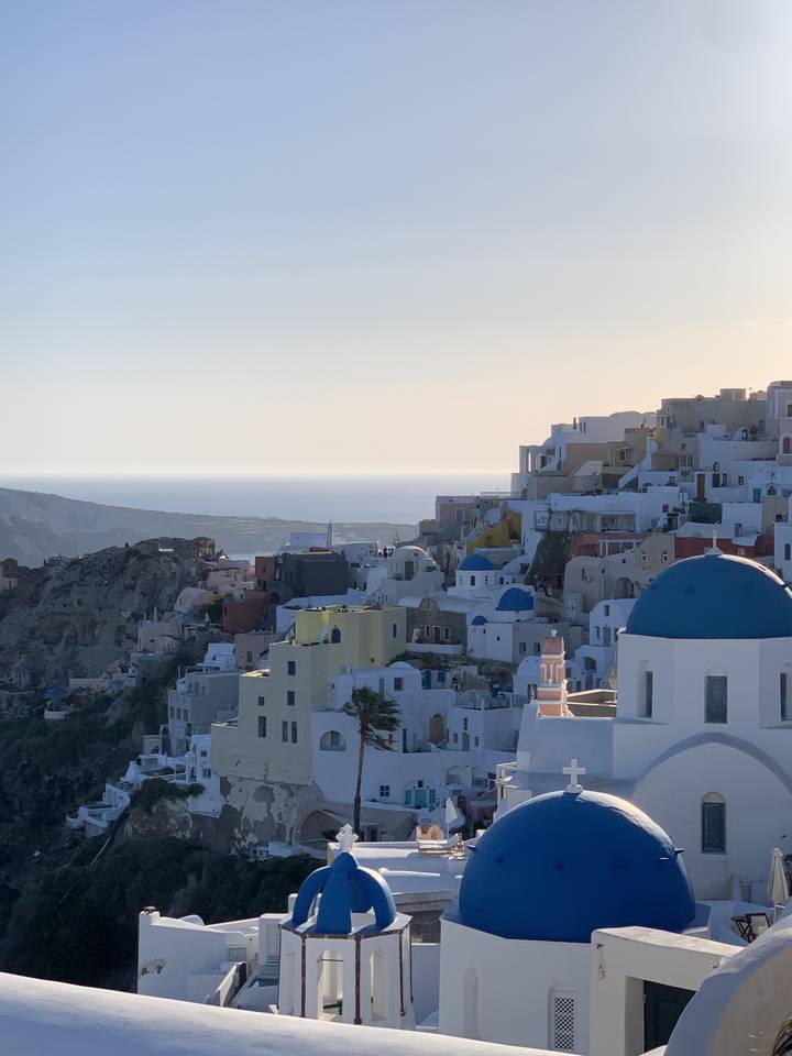 Vue de bâtiments blancs et aux couleurs pastel avec des dômes bleus sur une colline.