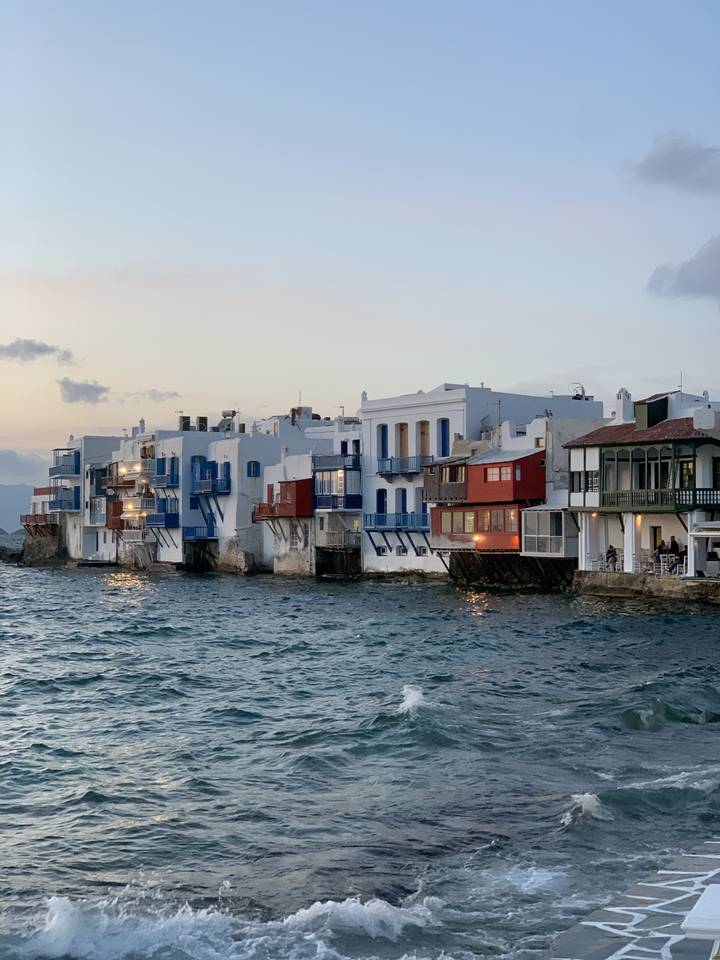 Vue bord de mer avec des bâtiments colorés et des vagues qui se brisent contre le rivage.