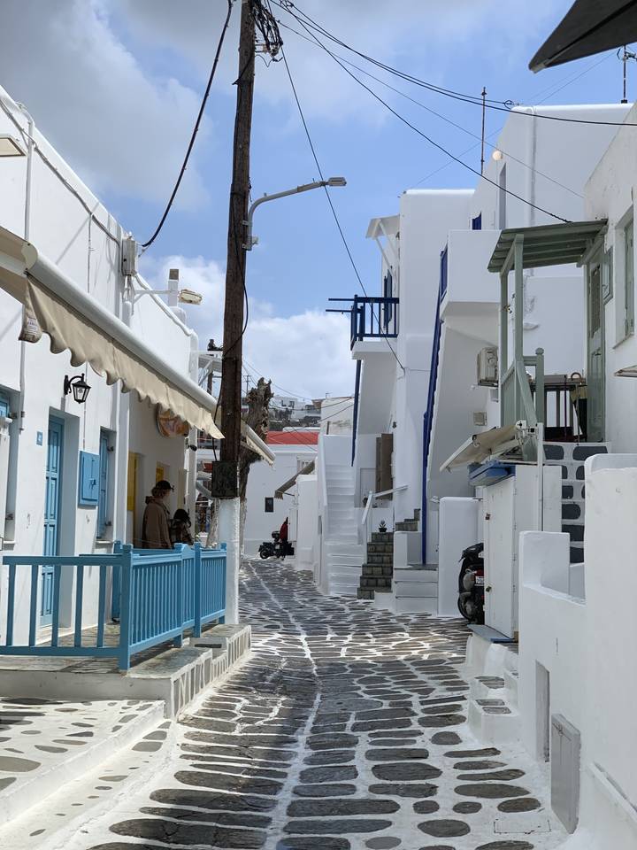 Rue étroite avec des bâtiments blancs et une chaise bleue au premier plan.