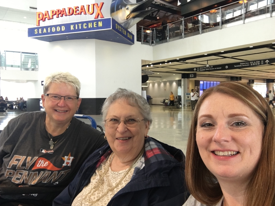 Trois personnes souriantes dans une zone d'attente d'aéroport.