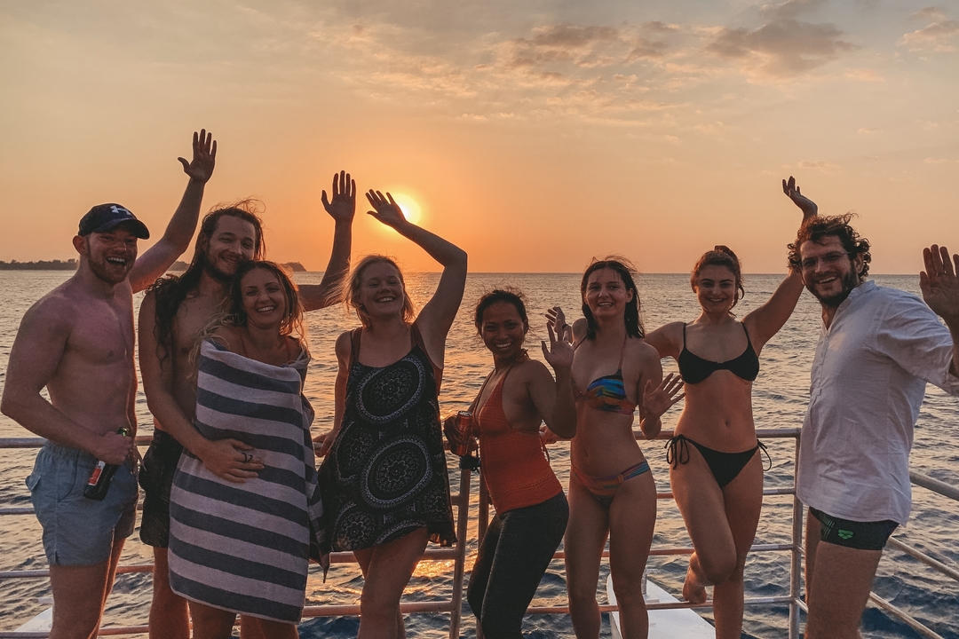 Groupe de personnes faisant signe au coucher du soleil sur un bateau.