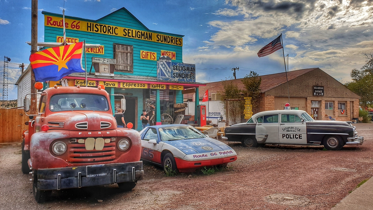 Panneau de la Route 66 historique avec des voitures anciennes et un magasin.