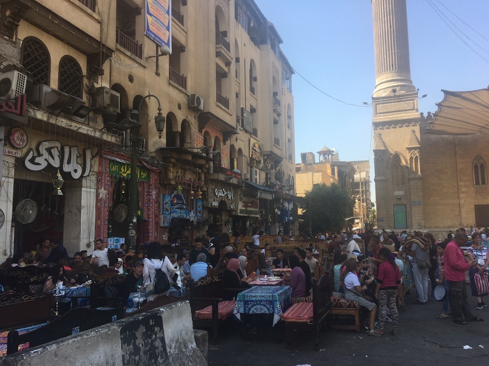 Rue marchande animée avec des tables et des boutiques.