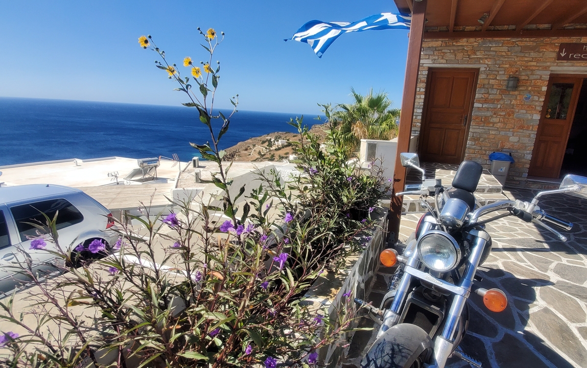 Vue sur mer avec moto, plantes et drapeau grec.