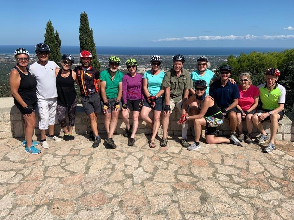 Groupe de cyclistes posant sur une plateforme de pierre avec vue sur la mer.