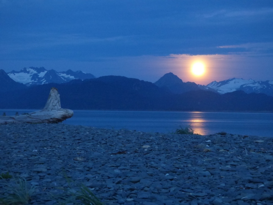 Lune se couchant sur une mer calme avec une chaîne de montagnes.
