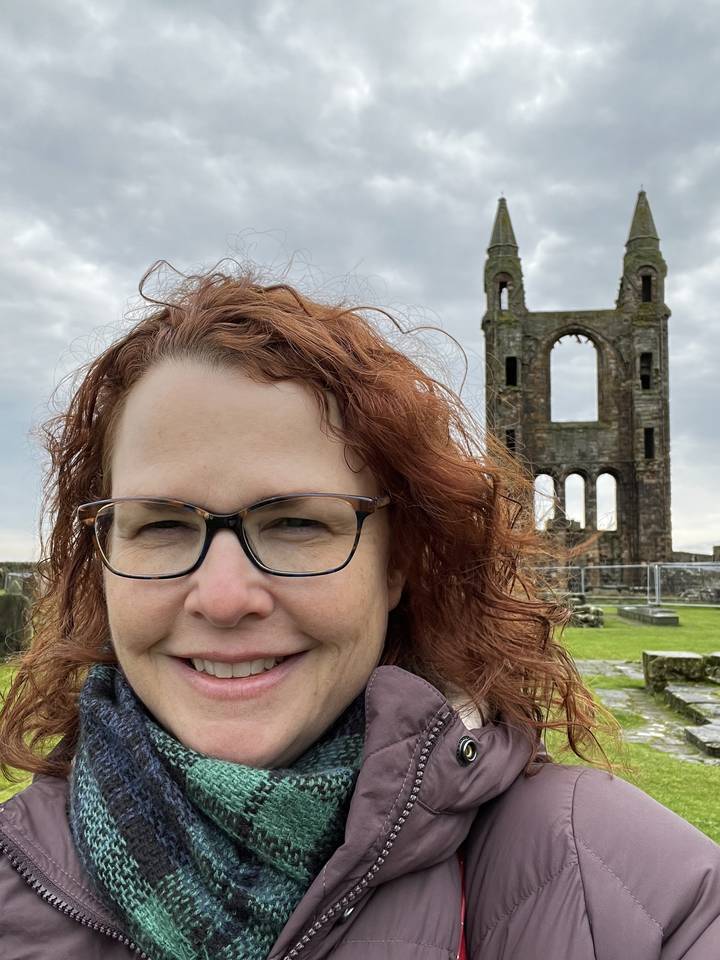 Personne aux cheveux bouclés devant une ruine en pierre.