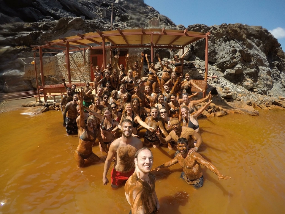 Large group covered in mud posing in a hot spring.