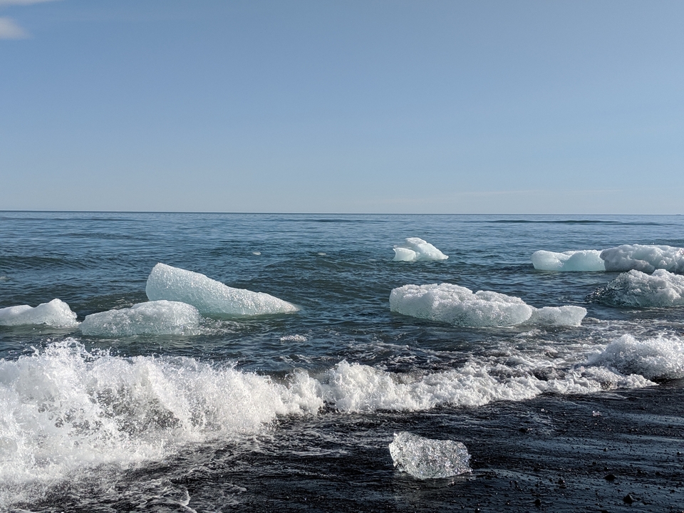 Icebergs floating in the ocean with waves crashing.