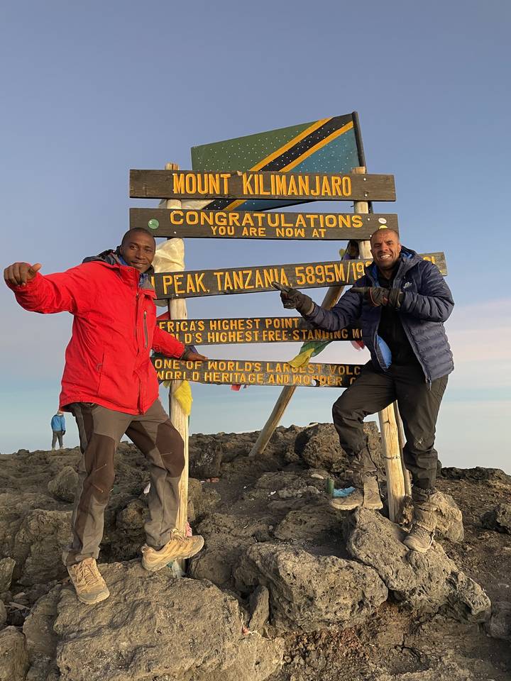 Deux personnes posant avec un panneau du mont Kilimandjaro au sommet.
