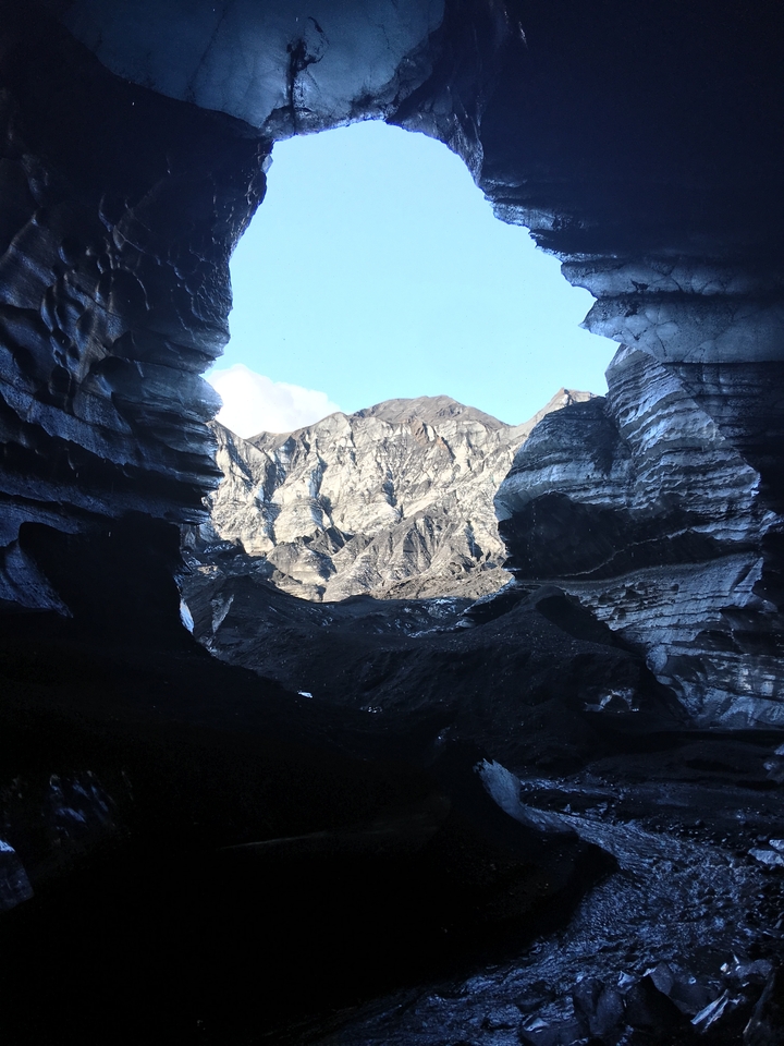 Ouverture de grotte rocheuse avec vue sur un paysage montagneux accidenté.