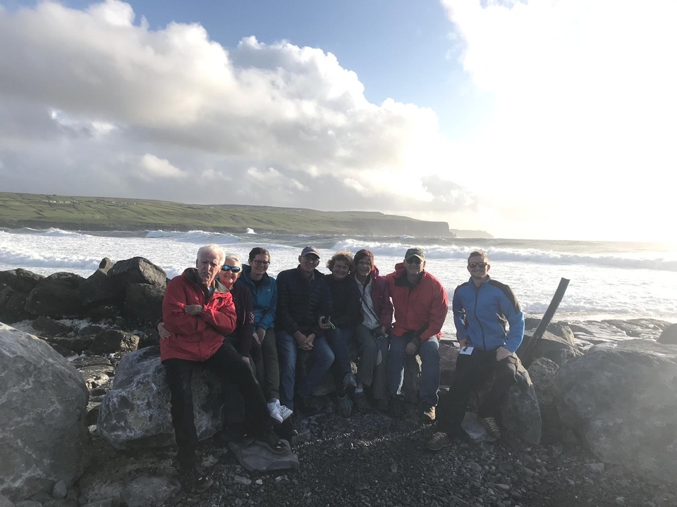 Groupe posant près d'un rivage rocheux avec des vagues qui se brisent derrière.