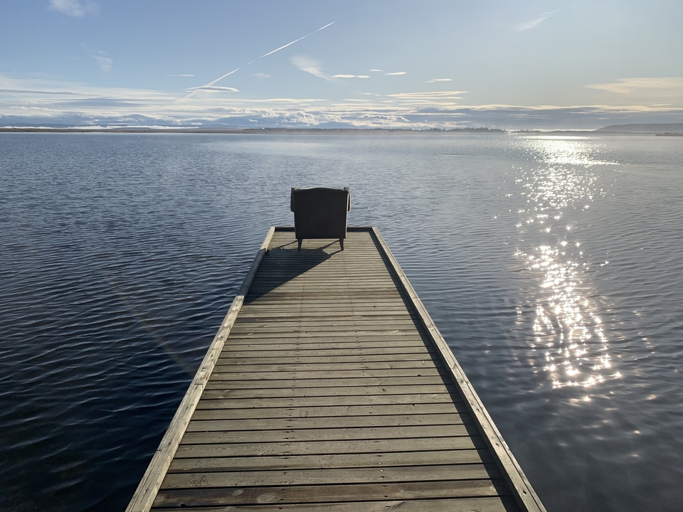 Dock extending into a lake with sun reflecting off water.